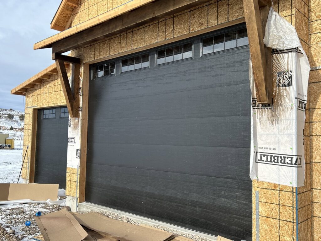 Two new dark grey garage doors installed on a house under construction, showcasing work by Delta Garage Door in Millcreek, UT.