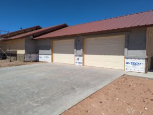 Two new light-colored panel garage doors installed on a house under construction by Precision Garage Door of Albuquerque and Santa Fe, NM.