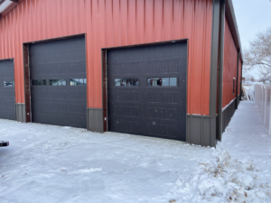 Two newly installed dark garage doors on a red metal building by Crafting Solutions MT LLC in Helena, MT