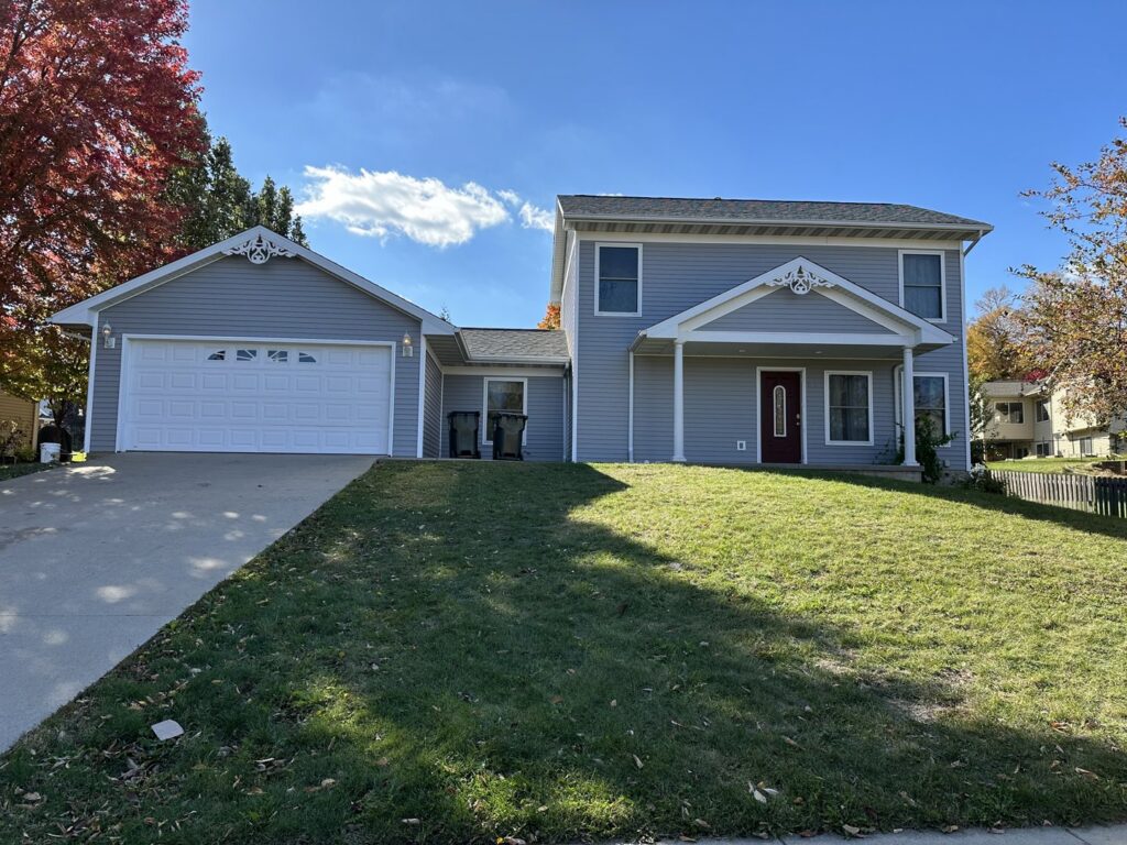 A residential home featuring new light blue siding and a white garage door, installed by DJ Paz All Siding & Roofing Construction in Iowa City, IA