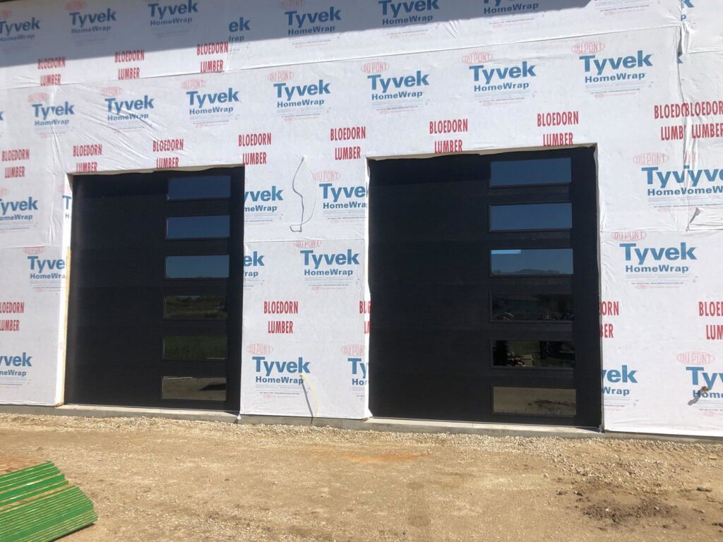 New modern black garage doors with multiple windows installed on a building under construction by Vertical Door Solutions in Sheridan, WY
