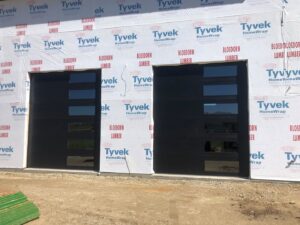 New modern black garage doors with multiple windows installed on a building under construction by Vertical Door Solutions in Sheridan, WY