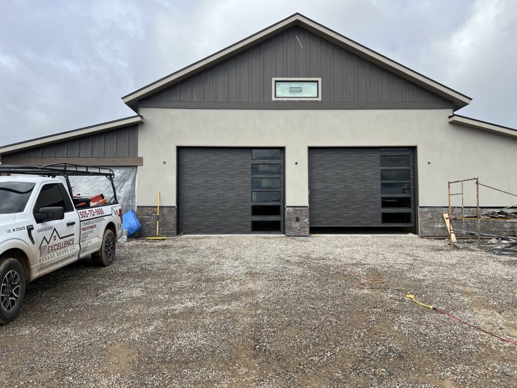 Two newly installed modern garage doors on a residential property by Excellence Garage Doors LLC in Albuquerque, NM, with a service truck nearby.