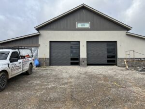 Two newly installed modern garage doors on a residential property by Excellence Garage Doors LLC in Albuquerque, NM, with a service truck nearby.