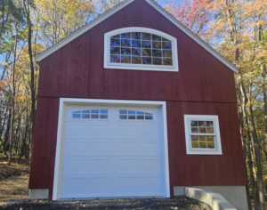 A newly installed white panel garage door on a red barn-style building by Champion Overhead Door in Brattleboro, VT.