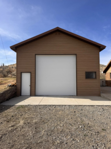 A newly installed white garage door on a brown building by Cowboy State Garage Doors, LLC in Cheyenne, WY.