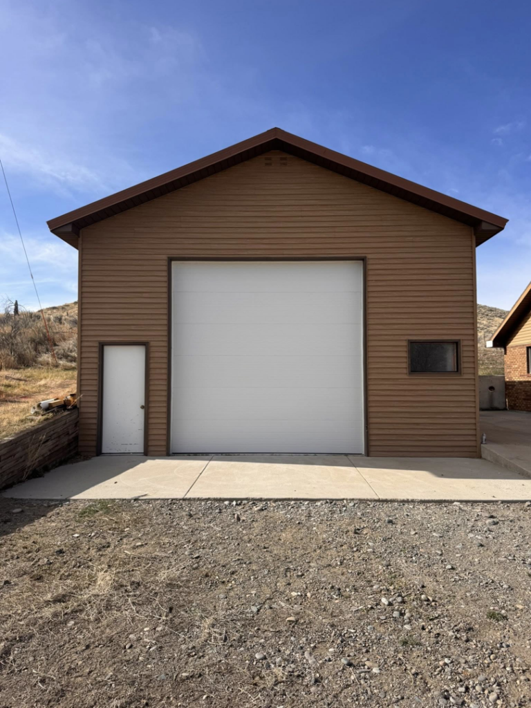 A newly installed white garage door on a brown building by Cowboy State Garage Doors, LLC in Cheyenne, WY.