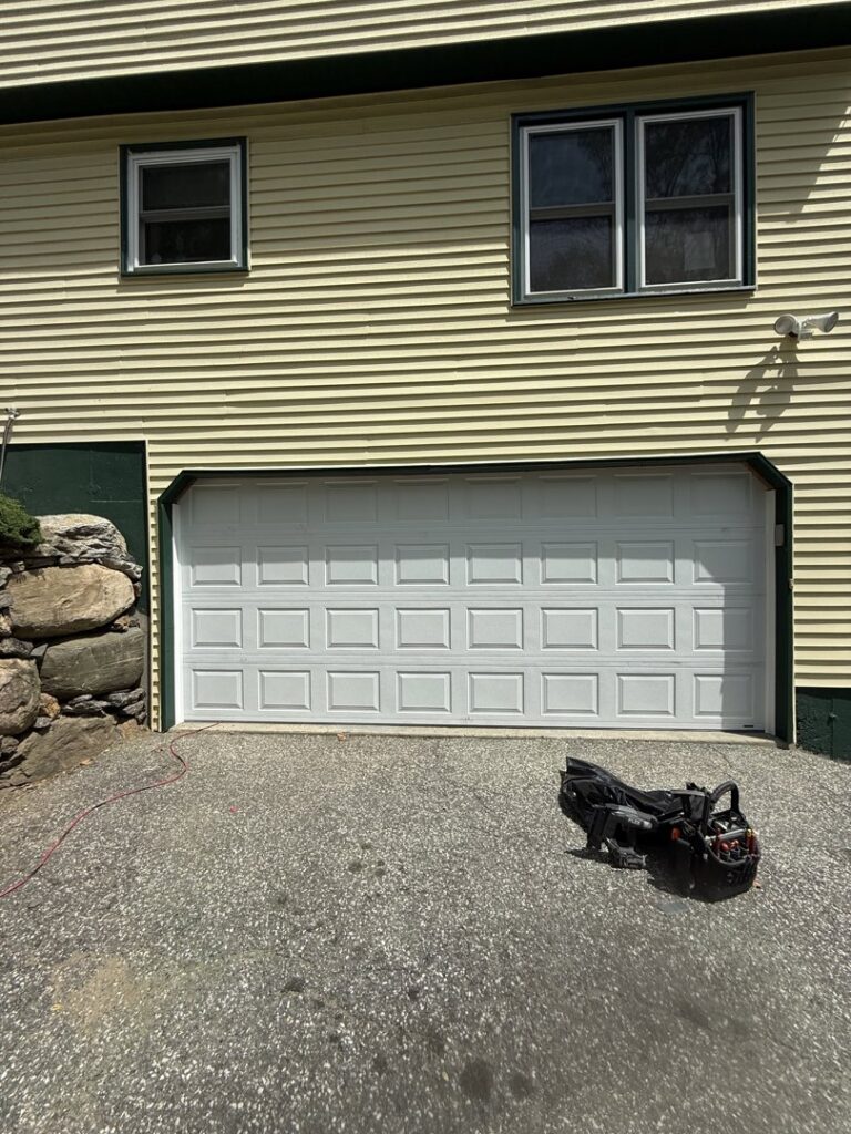 A newly installed white garage door on a yellow house by Mascolo Overhead Doors & Maintenance in Brookfield, CT.