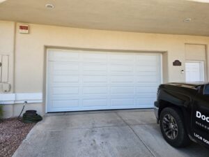 A newly installed white panel garage door on a house, with a work truck nearby, by Rebel Overhead Doors in Las Vegas, NV.