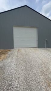 A newly installed white panel garage door on a modern grey metal building by 4thgenerationsdoors in Huntington, WV.