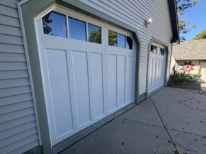 Two newly installed white garage doors with decorative windows on a residential home by Laramie Garage Doors in Laramie, WY.