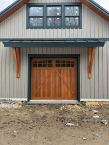 A newly installed wooden garage door with windows on a building by Ski Door, Inc. in Center Rutland, VT.