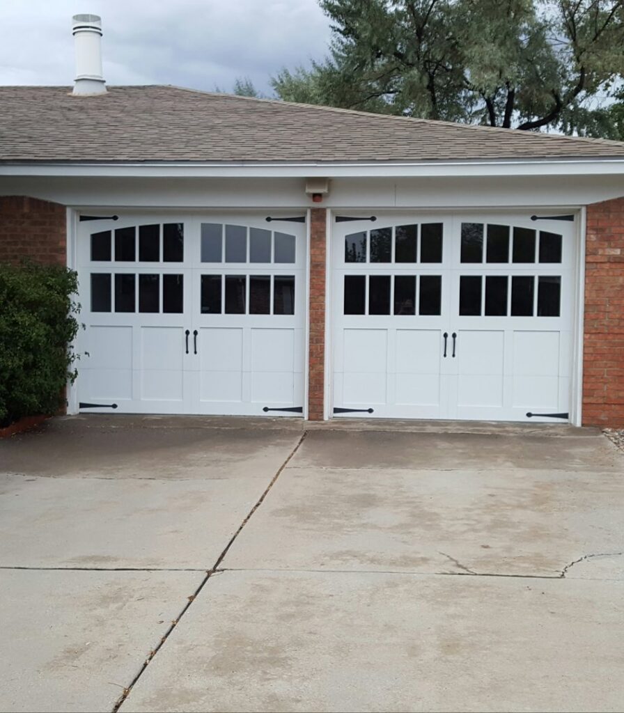 Newly installed white garage doors with decorative hardware on a brick house by Sandia Garage Door Repair in Albuquerque, NM
