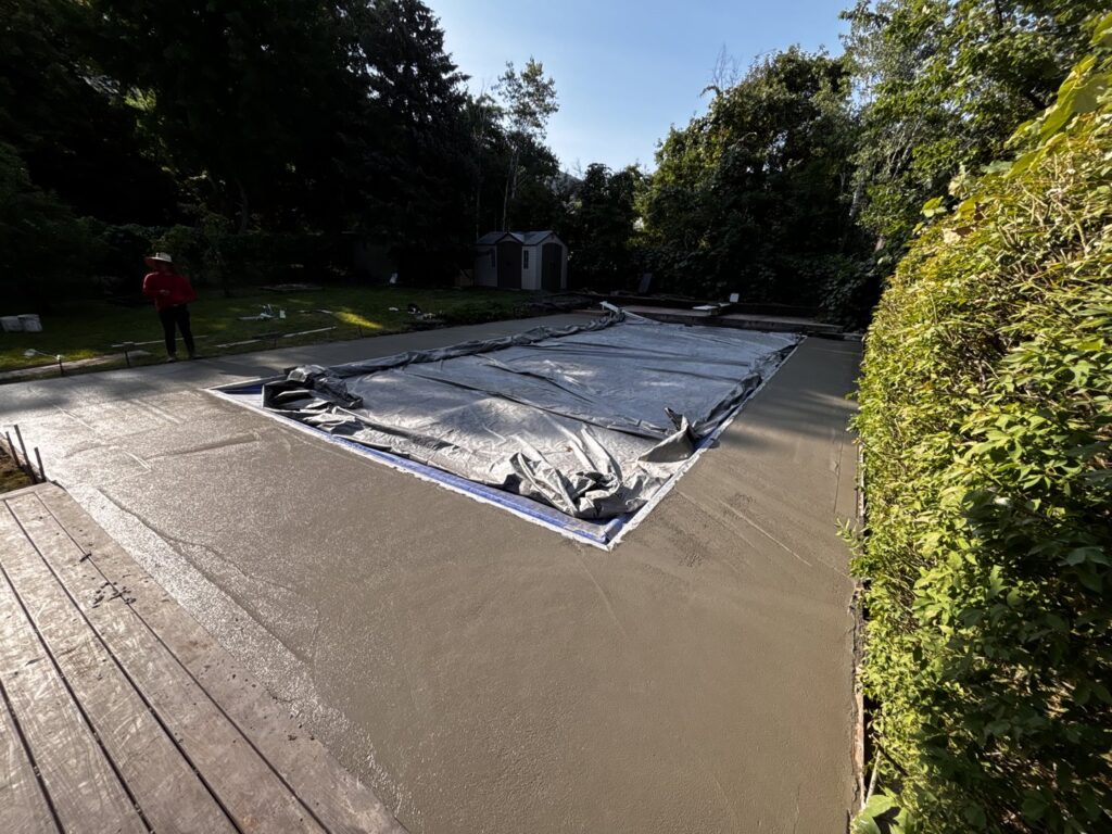 A newly poured concrete pool deck surrounding a covered swimming pool by Morton and Sons in Layton, UT