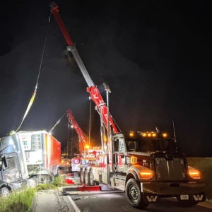 Two heavy-duty tow trucks from MAD J Repair & Towing performing a night recovery of a semi-truck in Des Moines, IA.