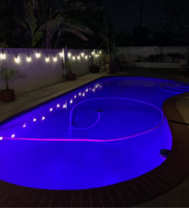 A pool cleaner hose working in a beautifully lit pool at night, providing service by Overflow Poolz LLC in Las Vegas, NV.