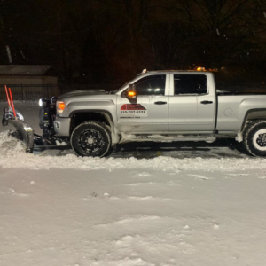 American Snow Removal LLC truck performing night snow plowing service, clearing snow from a lot in Des Moines, IA.