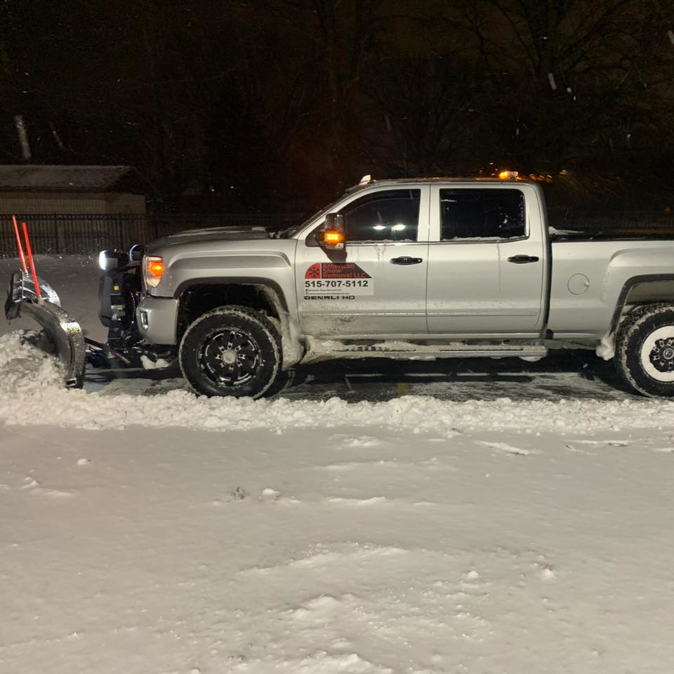 American Snow Removal LLC truck performing night snow plowing service, clearing snow from a lot in Des Moines, IA.