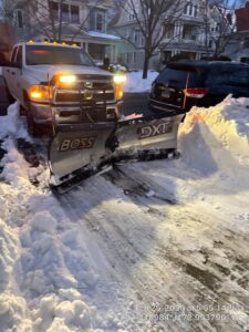 A white pickup truck with a snow plow clearing a snowy path at night, illuminated by headlights, by Diamond Image, New Haven, CT.