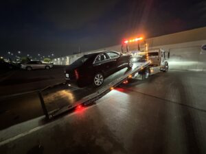 AJ's Towing Services & Roadside Assistance flatbed tow truck with a black sedan on its bed at night in Sacramento, CA.