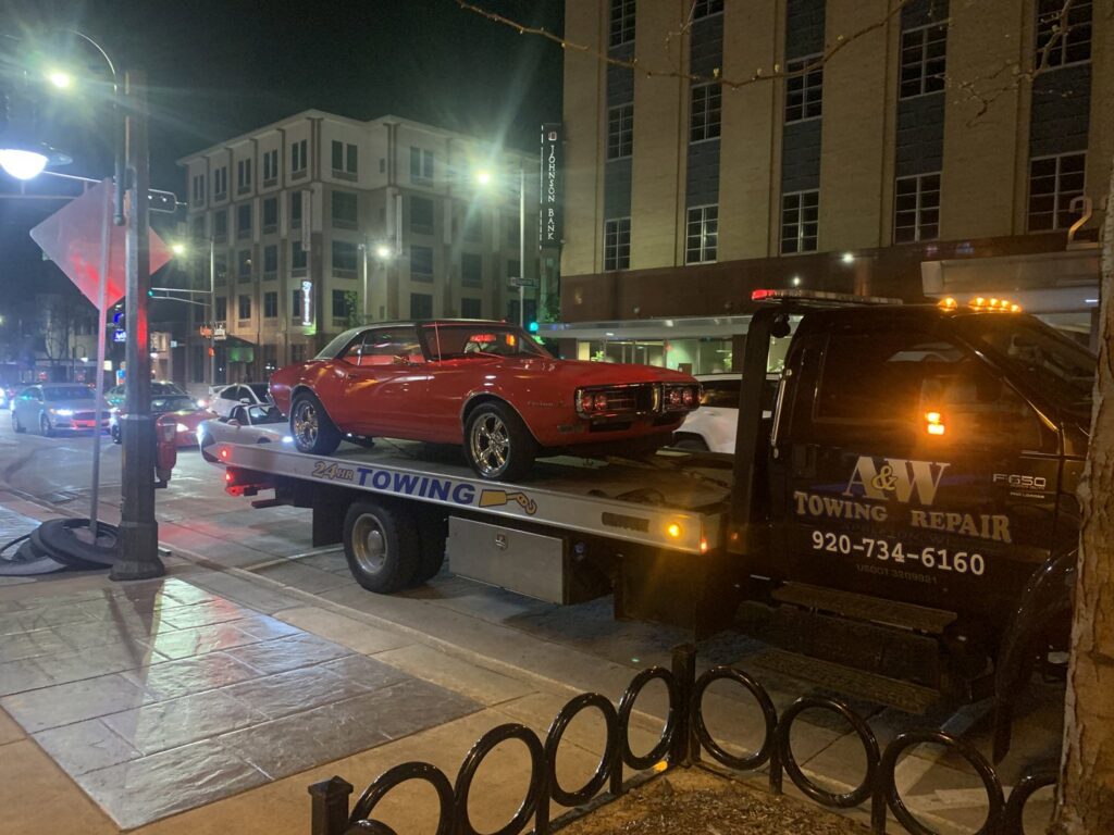 A&W Towing and Repair flatbed tow truck towing a classic red car at night in Appleton, WI.