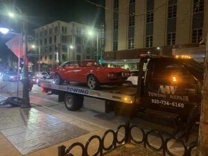 A&W Towing and Repair flatbed tow truck towing a classic red car at night in Appleton, WI.