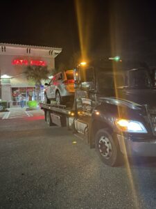 A black flatbed tow truck from Always Ready Towing transporting a silver SUV at night in North Fort Myers, FL.