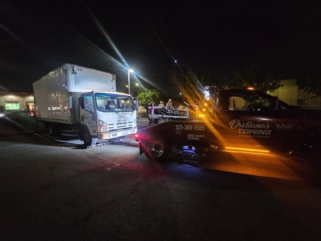 Orellanas Towing & Junk Car tow truck actively towing a white box truck at night in Los Angeles, CA.
