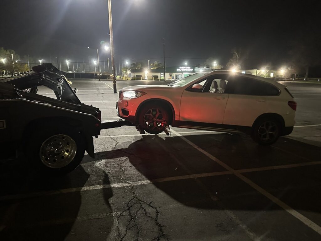 A white SUV being towed at night by a wheel lift tow truck by R towing Services in Sacramento, CA.