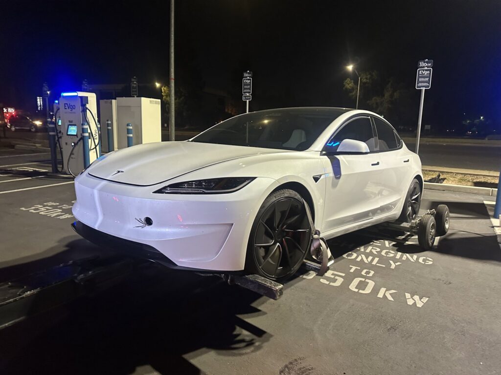 A white Tesla car being towed at night by a wheel lift tow truck with dollies by R towing Services in Sacramento, CA.