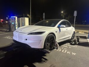A white Tesla car being towed at night by a wheel lift tow truck with dollies by R towing Services in Sacramento, CA.