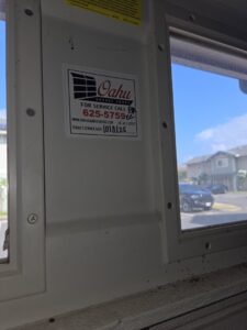 An Oahu Garage Doors service sticker with contact information on a garage door window frame in Waipahu, HI
