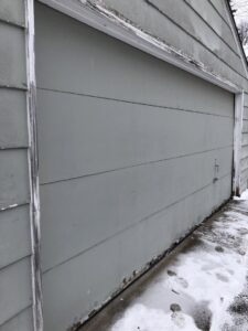 Old garage with damaged and peeling siding, showing need for repair by Capital Siding, Windows & Roofing, Woodbury, MN.