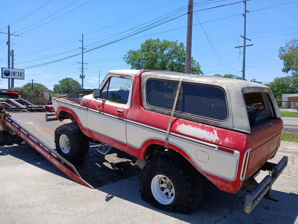 An old red and white Ford Bronco being loaded onto a flatbed tow truck from Rick's Towing and Recovery in Lafayette, LA.