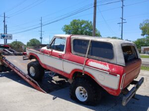 An old red and white Ford Bronco being loaded onto a flatbed tow truck from Rick's Towing and Recovery in Lafayette, LA.
