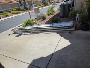 Old garage door panels and hardware stacked on a driveway after a replacement job by Rebel Overhead Doors in Las Vegas, NV.