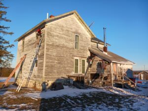 An old house with weathered siding and ladders, indicating siding repair or replacement work by Murphy Builders- Genesee County in Ossineke, MI.