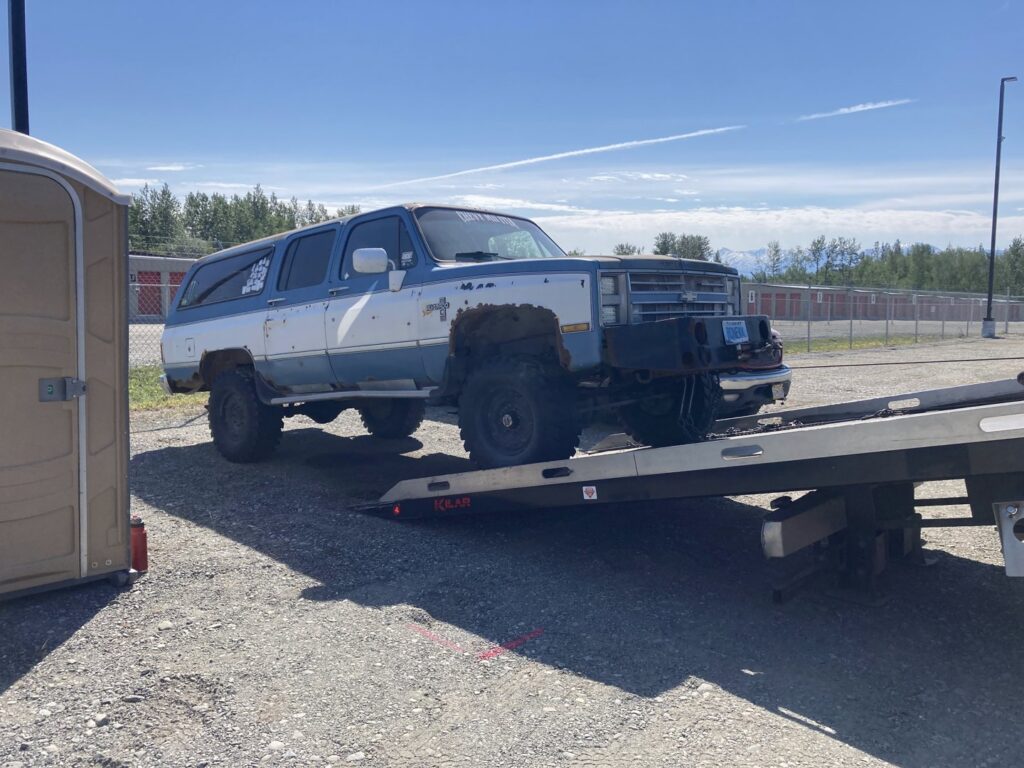 An old, lifted SUV being loaded onto a flatbed tow truck by AK Car Crushing & Recycling & ACCR Towing in Wasilla, AK.