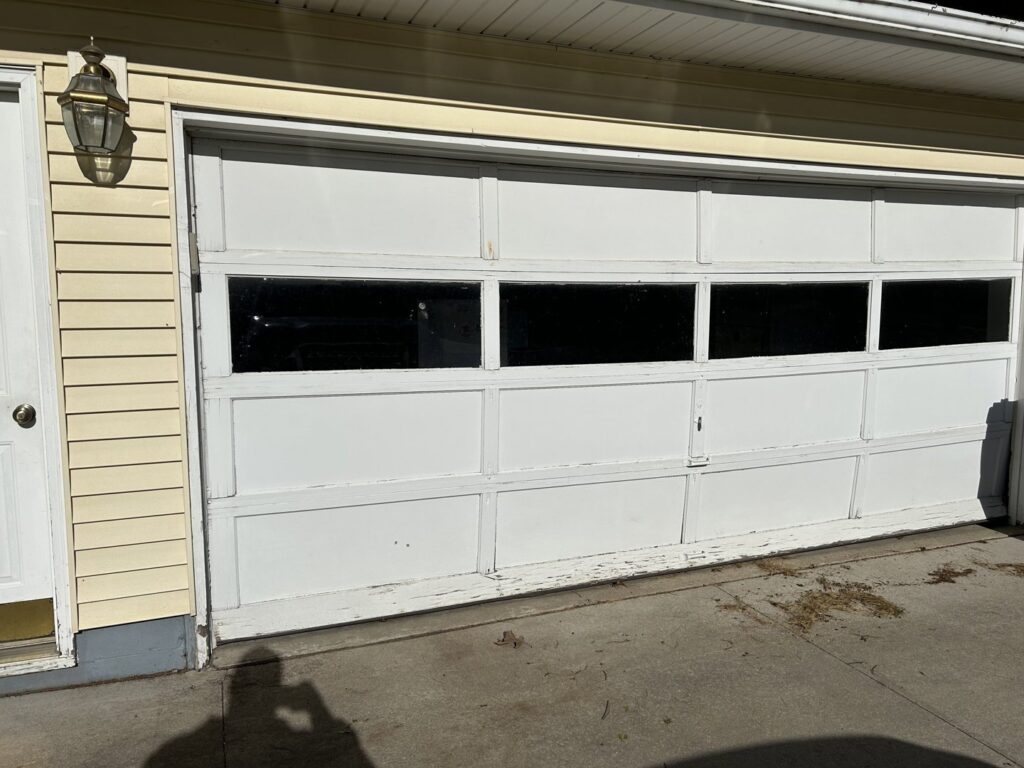 Old white garage door with peeling paint, ready for replacement by Cedar Valley Garage Doors in Waterloo, IA