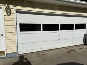 Old white garage door with peeling paint, ready for replacement by Cedar Valley Garage Doors in Waterloo, IA