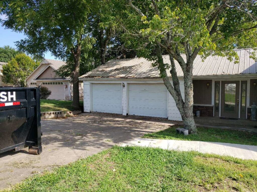 Older white garage doors on a house, indicating potential replacement or repair service by Garage Doors & More in Bentonville, AR