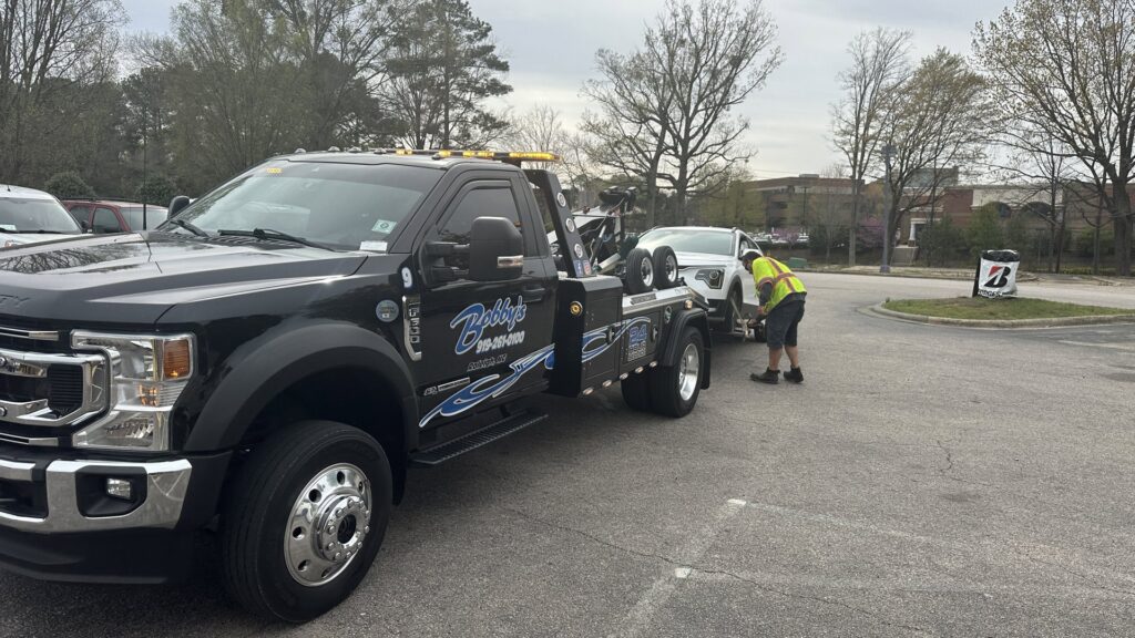 A Bobbys Towing & Recovery operator loading a white car onto a flatbed tow truck in Raleigh, NC.
