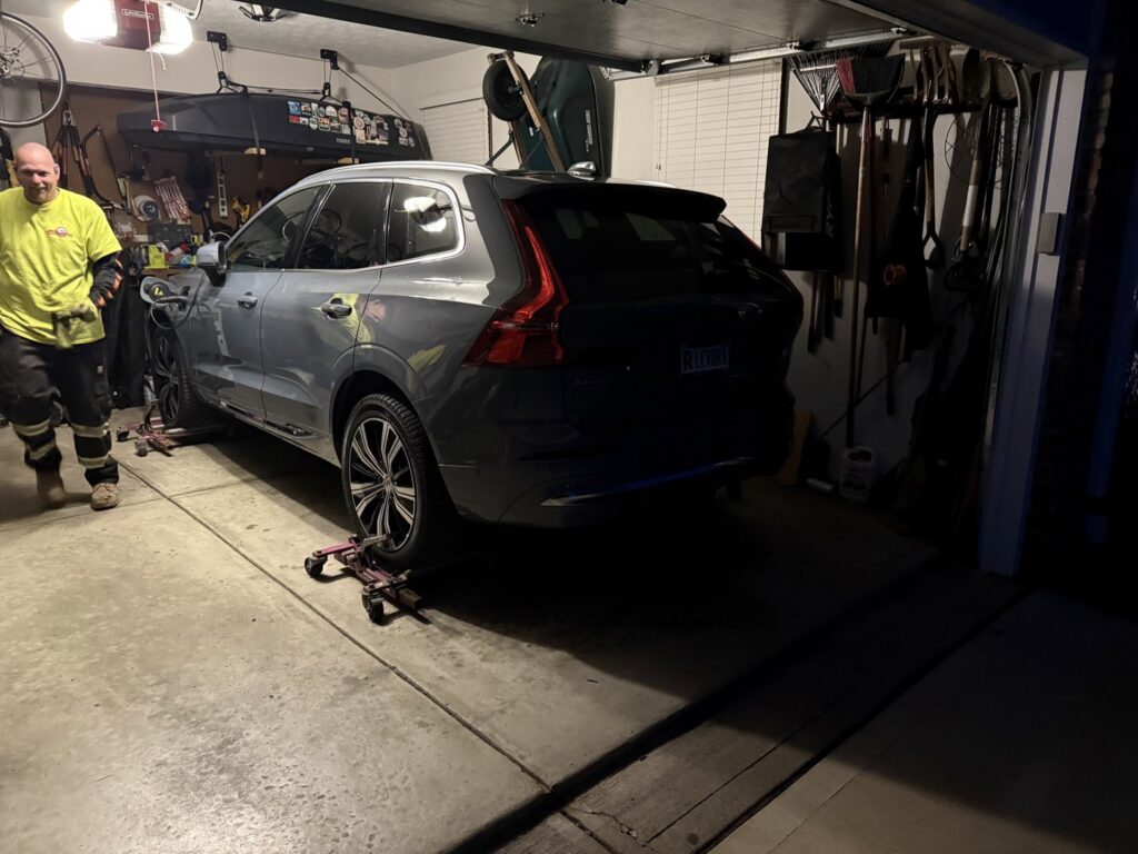 A tow truck operator moving a grey SUV with wheel dollies in a garage, part of recovery services by JR's Services and Recovery, LLC in Indianapolis, IN.