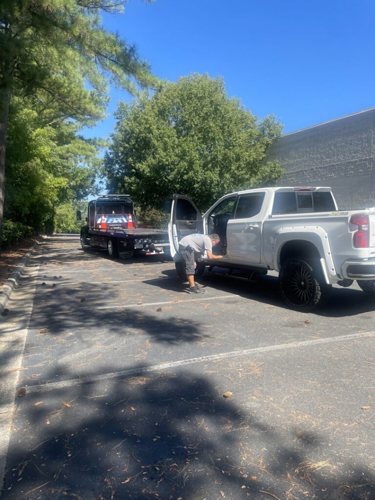 A Bobbys Towing & Recovery operator securing a white pickup truck onto a flatbed tow truck in Raleigh, NC.