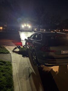 A tow truck operator securing a grey SUV onto a flatbed tow truck at night, providing towing services by JR's Services and Recovery, LLC in Indianapolis, IN.