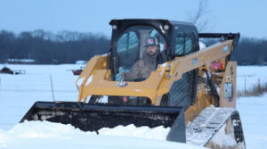 An operator in a CAT skid steer loader plowing snow from a large, open area for AMK Forestry in Conway, AR.