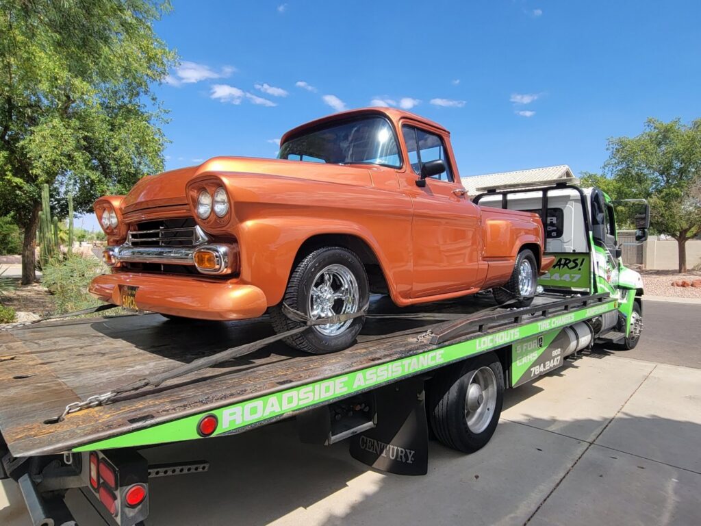 An orange classic pickup truck being transported on a flatbed tow truck by Caliber Towing in Phoenix, AZ.