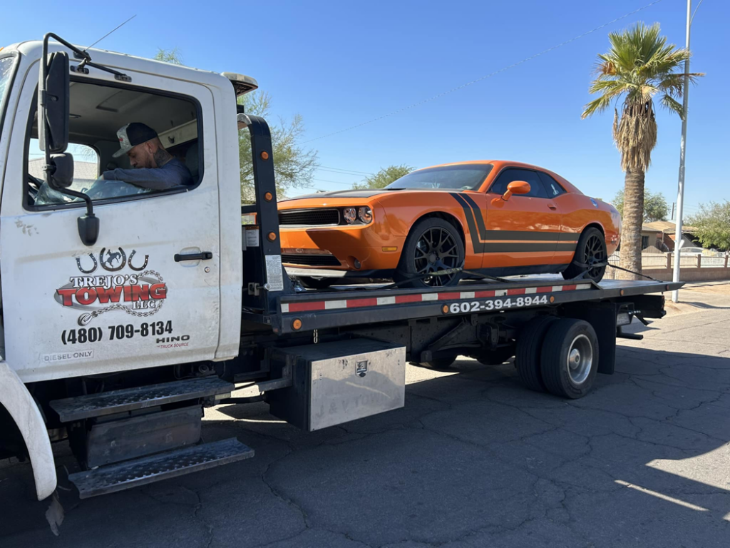 An orange Dodge Challenger being transported on a flatbed tow truck by Trejo's Towing LLC in Phoenix, AZ.