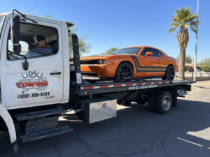 An orange Dodge Challenger being transported on a flatbed tow truck by Trejo's Towing LLC in Phoenix, AZ.