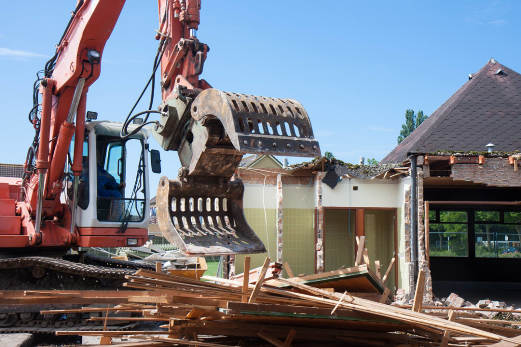 An orange excavator with a grapple attachment demolishing a building for San Antonio Demolition Pros in San Antonio, TX.